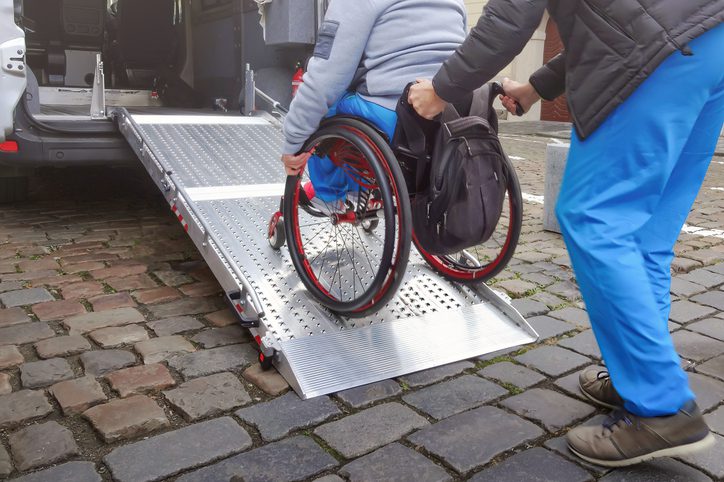 Person in wheelchair using a metal ramp on cobblestone street.