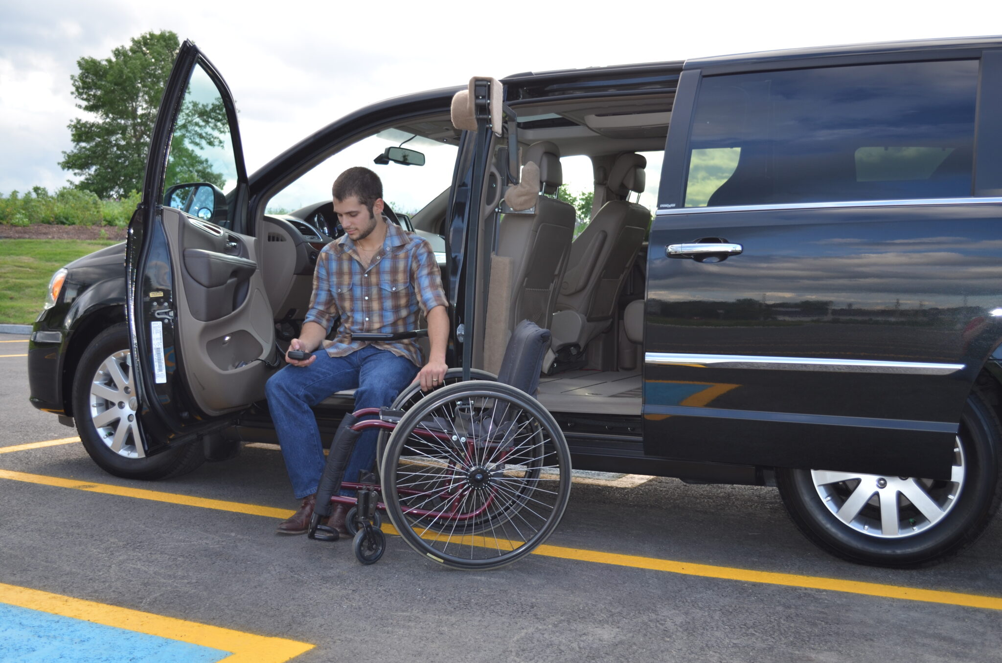 Man transferring from wheelchair to accessible van in parking lot.