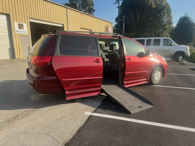 Red wheelchair-accessible van with ramp extended in parking lot.