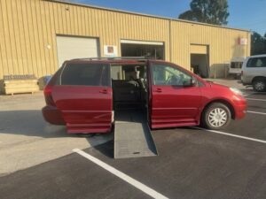 Red wheelchair-accessible van with ramp deployed outside a building.