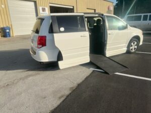 White wheelchair-accessible van with ramp extended outside a building.