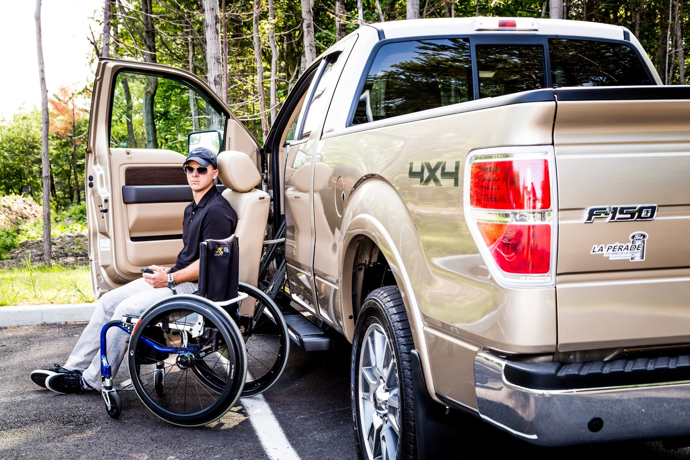 A woman in a wheelchair beside a pickup truck outdoors.