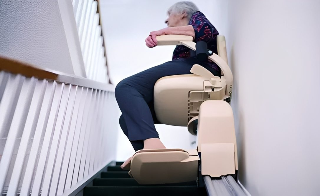 Person sitting on a stair lift chair near a railing.
