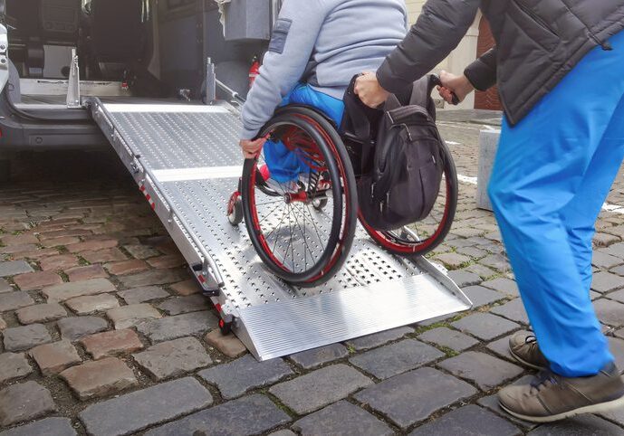 Person in wheelchair using a metal ramp on cobblestone street.