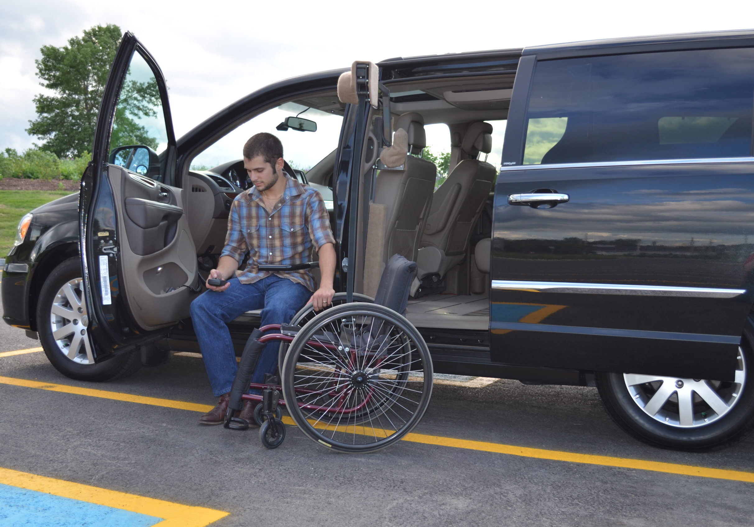 Man transferring from wheelchair to accessible van in parking lot.