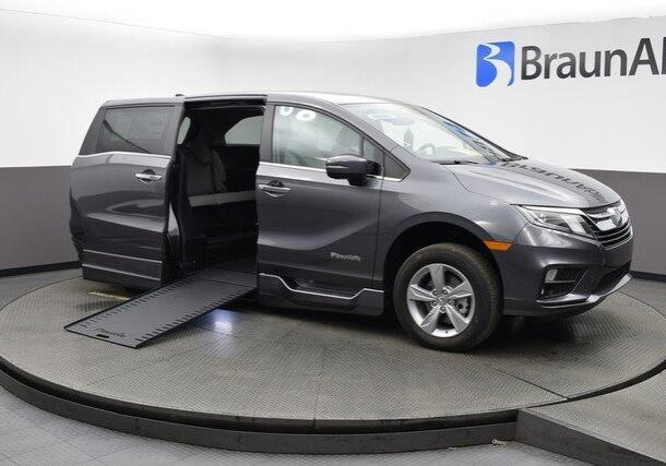 Black wheelchair-accessible van with ramp deployed on showroom floor.