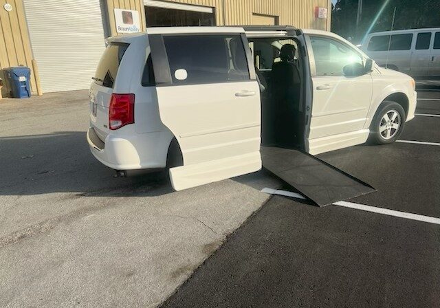 White wheelchair-accessible van with ramp extended outside a building.